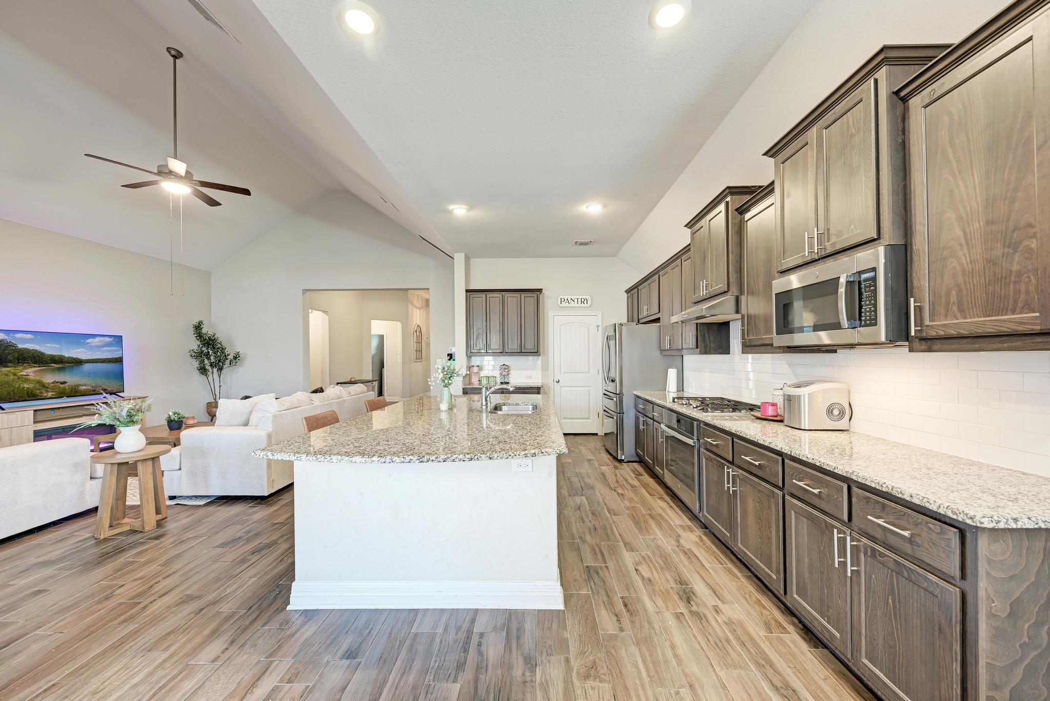 198 Rough Leaf Drive Buda, TX 78610 - Photo 14 of 38 Kitchen with stainless steel appliances, light wood-type flooring, light stone countertops, a ceiling fan, and a kitchen island with sink