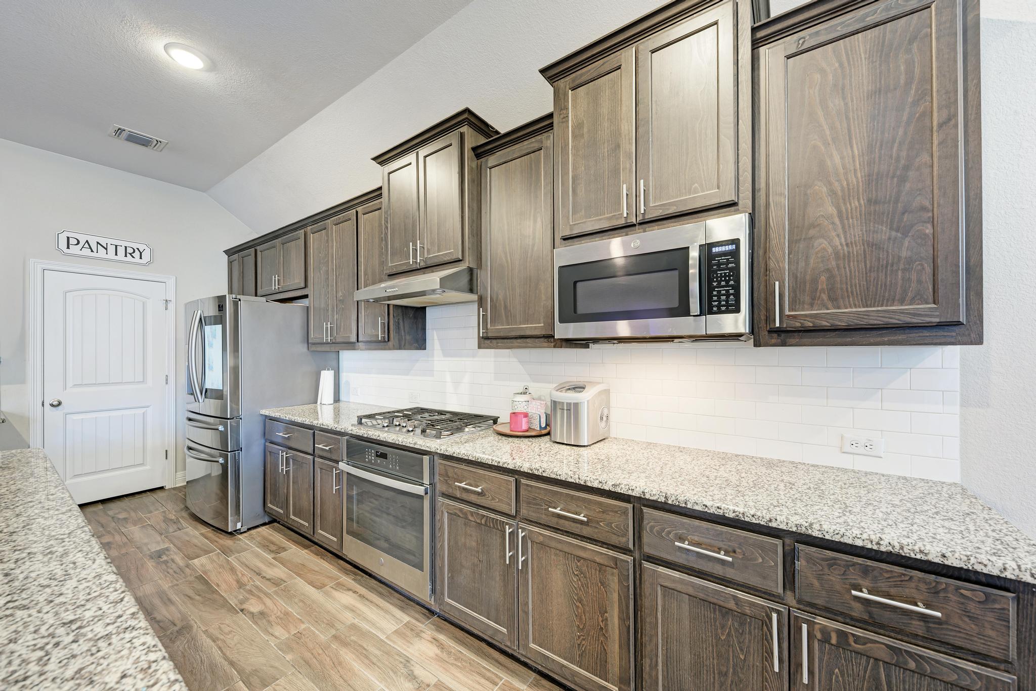 198 Rough Leaf Drive Buda, TX 78610 - Photo 15 of 38 Kitchen featuring dark wood finish cabinets, stainless steel appliances, vaulted ceiling, light stone counters, and light wood finished floors