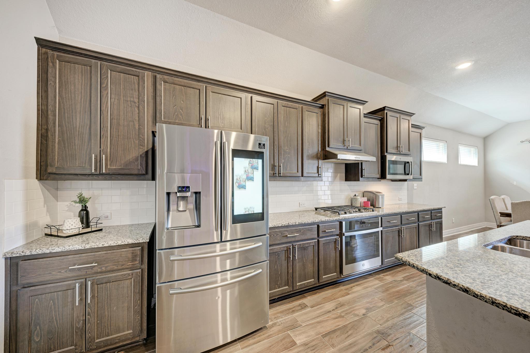 198 Rough Leaf Drive Buda, TX 78610 - Photo 16 of 38 Kitchen with stainless steel appliances, light stone counters, lofted ceiling, wood finish floors, and dark wood finish cabinets