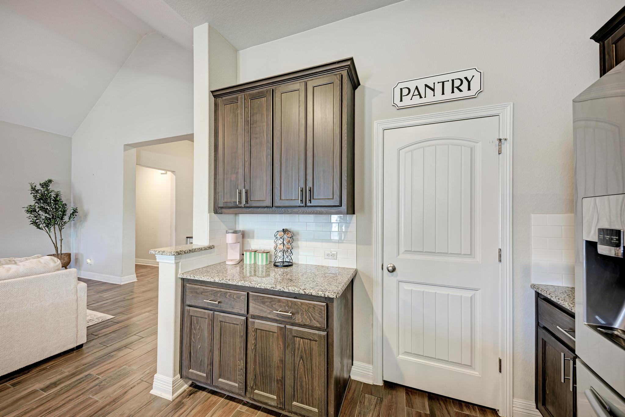 198 Rough Leaf Drive Buda, TX 78610 - Photo 38 of 38 Kitchen featuring tasteful backsplash, light stone countertops, dark wood finish cabinetry, open floor plan, and stainless steel refrigerator with ice dispenser