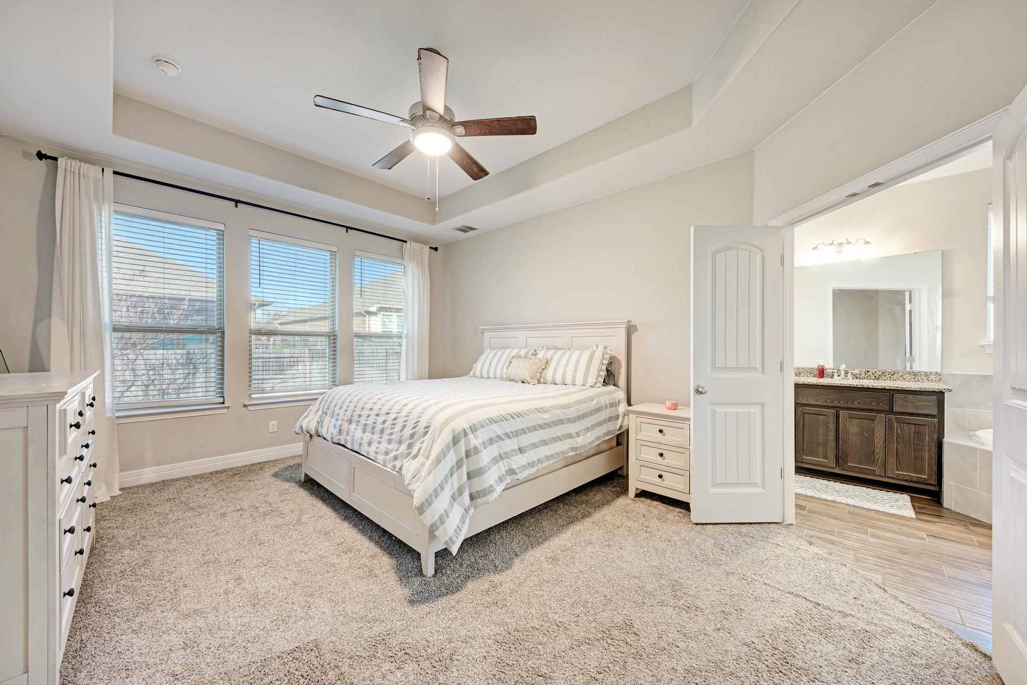 198 Rough Leaf Drive Buda, TX 78610 - Photo 18 of 38 Bedroom with a tray ceiling, a ceiling fan, light colored carpet, and ensuite bathroom