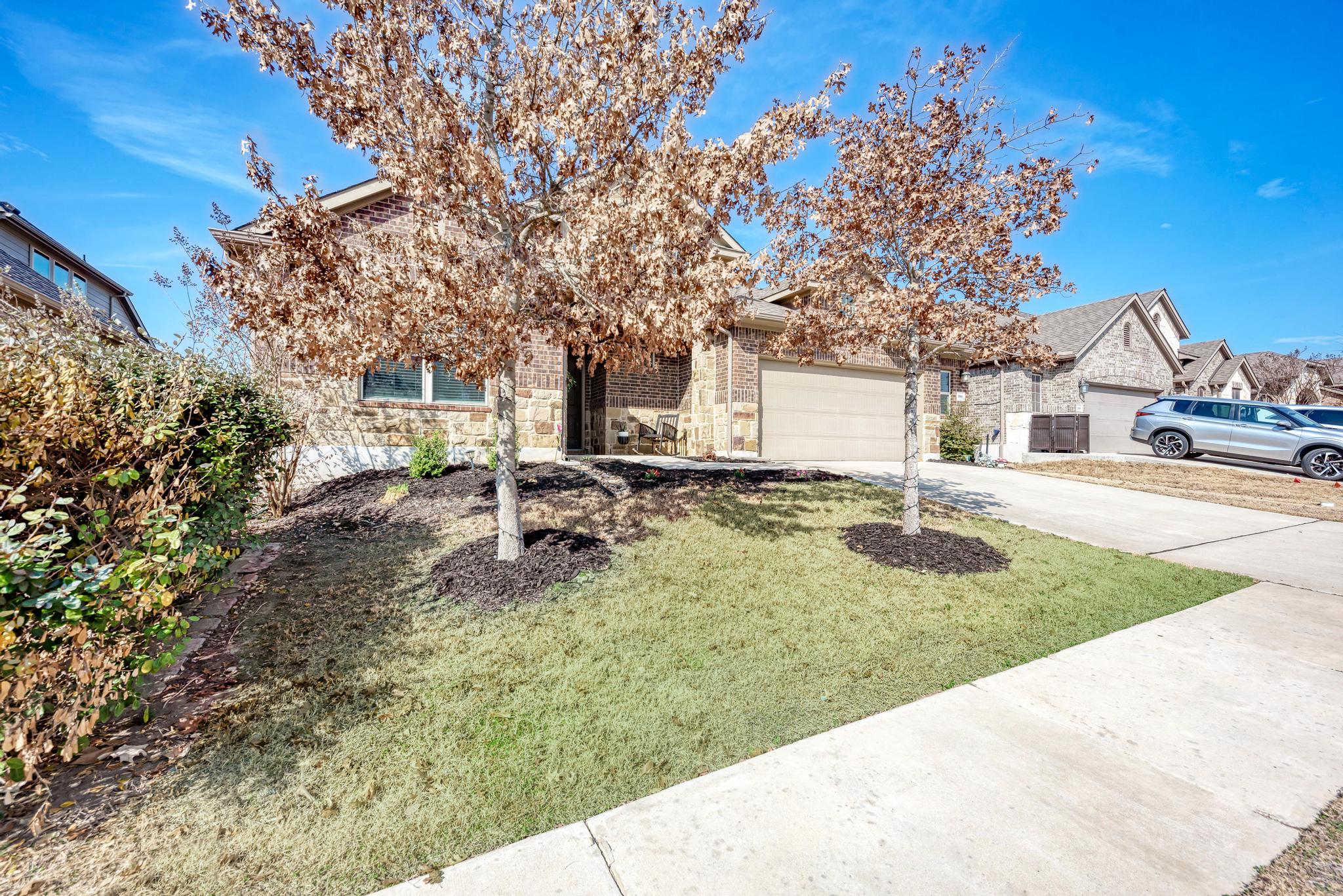198 Rough Leaf Drive Buda, TX 78610 - Photo 4 of 38 View of property hidden behind natural elements featuring concrete driveway, stone siding, an attached garage, and a front yard