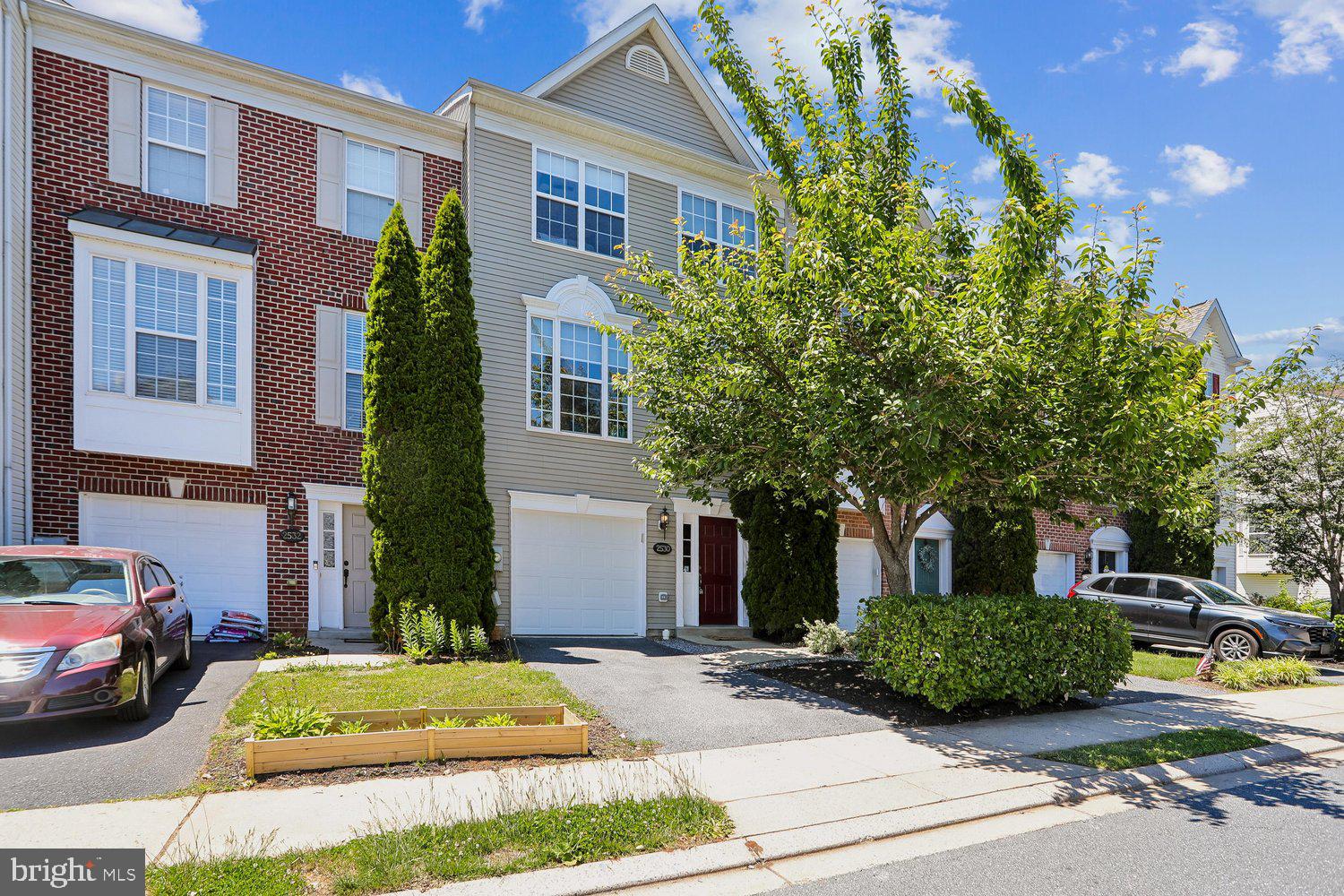 a view of a brick house with a yard plants and large tree