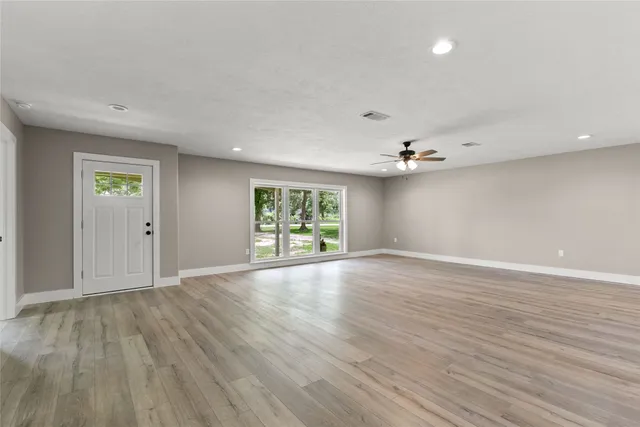 an empty room with wooden floor chandelier and windows