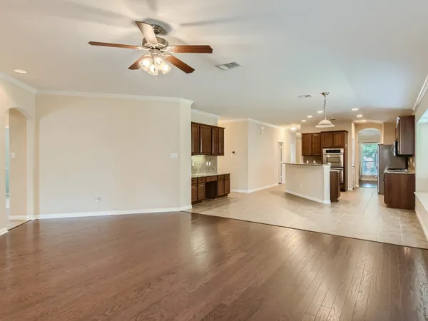 a view of a big room with wooden floor a kitchen view and a chandelier fan