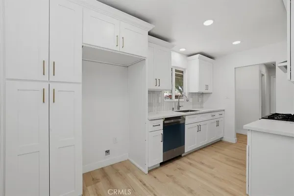 a kitchen with stainless steel appliances granite countertop a sink a stove a refrigerator and white cabinets with wooden floor