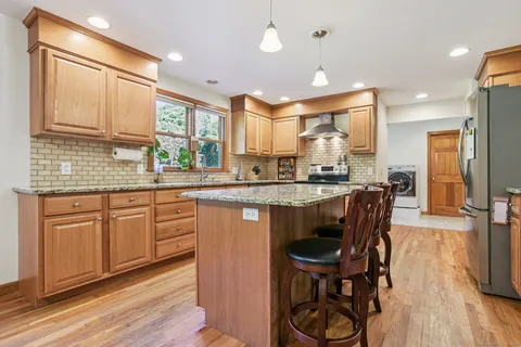 a kitchen with stainless steel appliances granite countertop a stove a sink dishwasher a microwave oven and a dining table with wooden floor