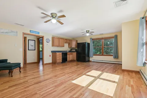 a view of an empty room with window wooden floor and a kitchen view