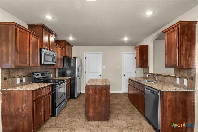 a kitchen with stainless steel appliances granite countertop wooden cabinets a sink dishwasher a stove and a refrigerator