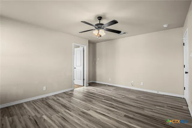 a view of an empty room with wooden floor and a ceiling fan