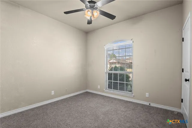 an empty room with chandelier fan and windows