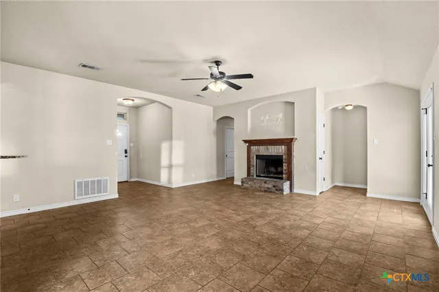 a view of an empty room with chandelier fan and fire place