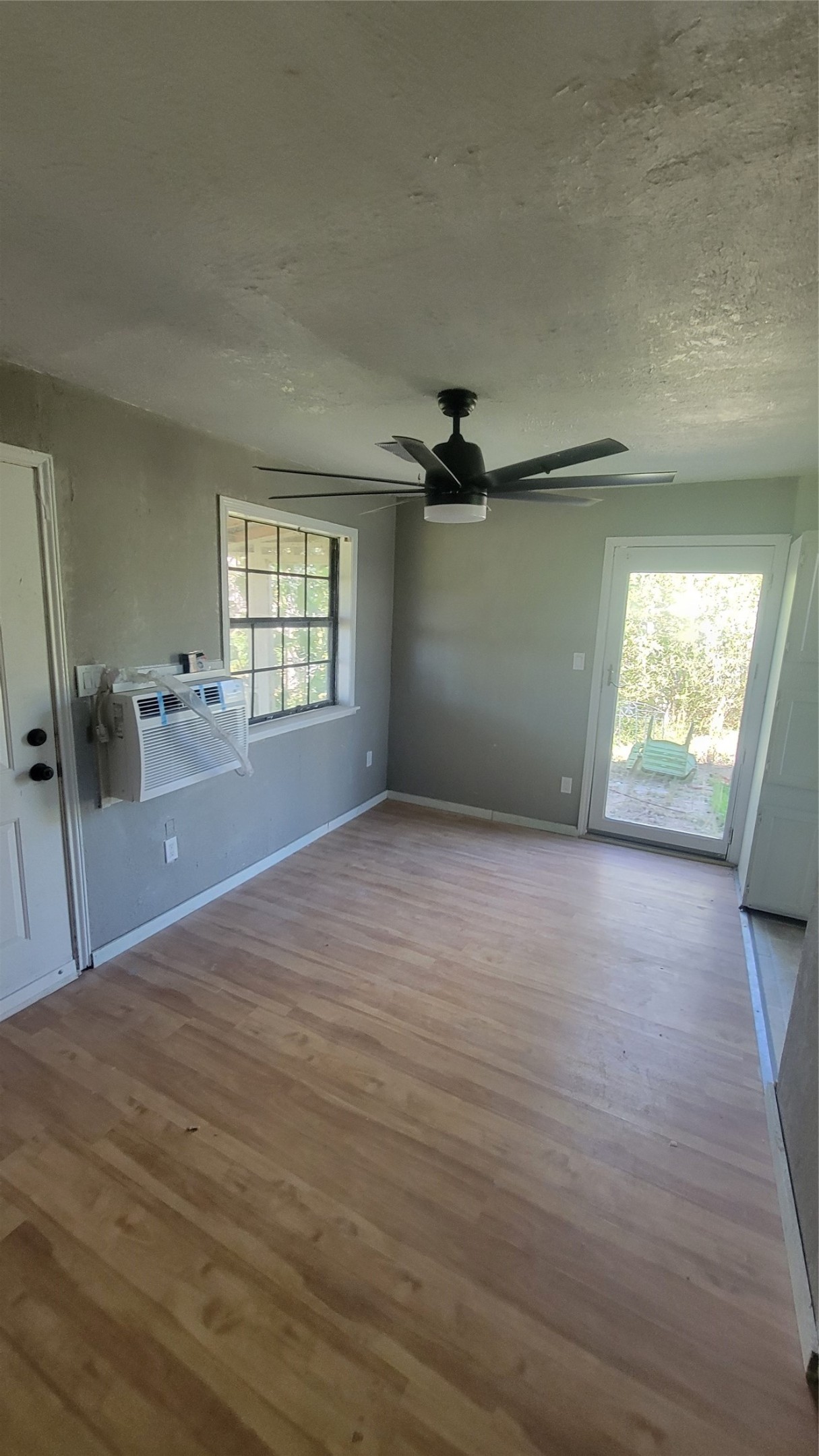12018 Sandpiper Road Angleton, TX 77515 - Photo 32 of 48 This room features hardwood floors, a ceiling fan, and a wall-mounted air conditioning unit. It has a window for natural light and a door leading to an outdoor area. Ideal for a cozy living space or office.