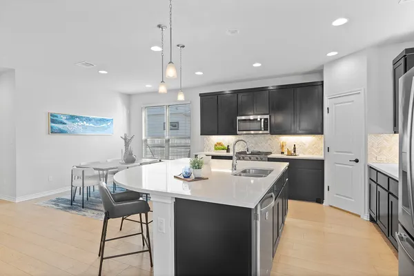 a kitchen with stainless steel appliances kitchen island granite countertop a sink a stove a refrigerator a dining table and chairs