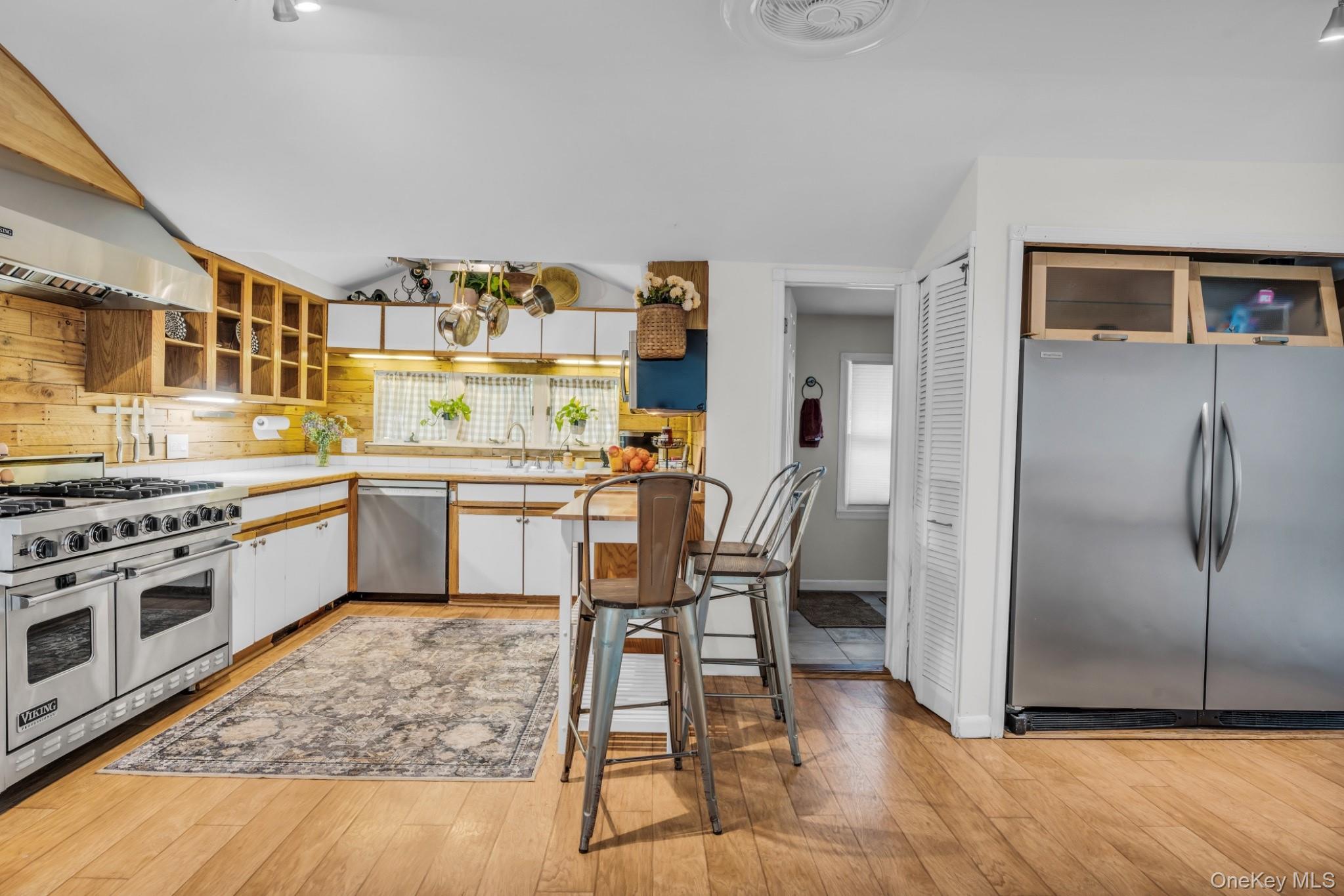64 Sally Lane Ridge, NY 11961 - Photo 1 of 18 Kitchen featuring appliances with stainless steel finishes, light countertops, glass insert cabinets, white cabinetry, and light wood-type flooring