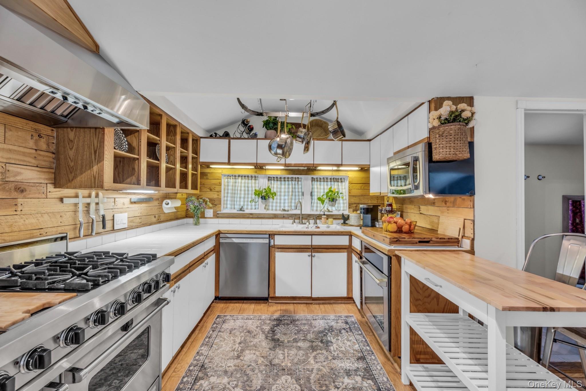 64 Sally Lane Ridge, NY 11961 - Photo 6 of 18 Kitchen featuring stainless steel appliances, white cabinetry, ventilation hood, light wood-style flooring, and vaulted ceiling