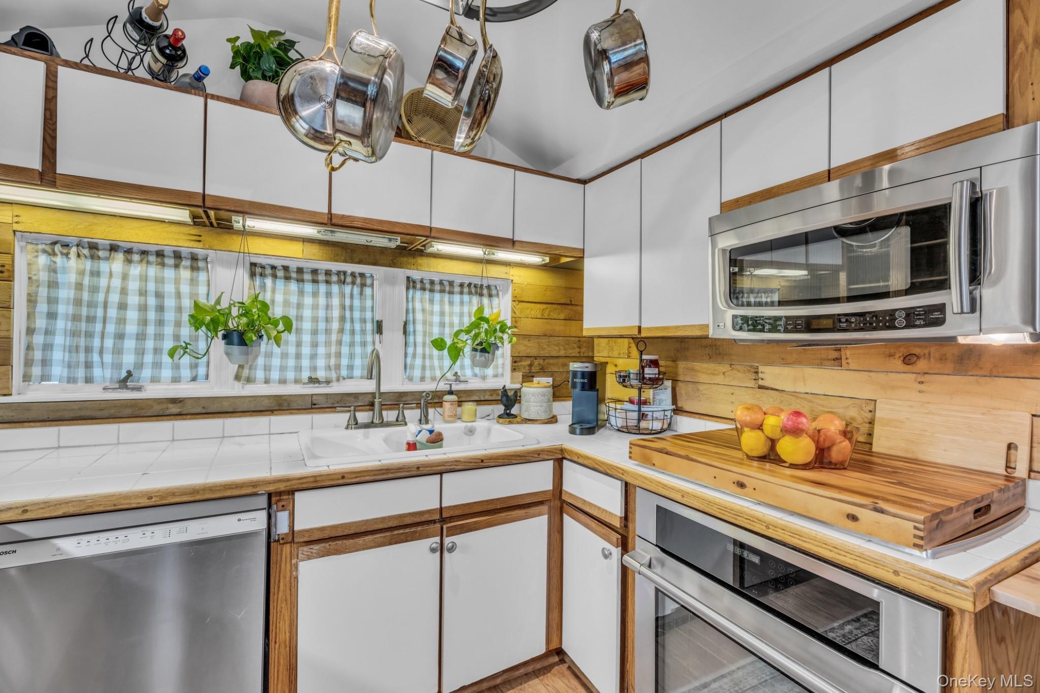 64 Sally Lane Ridge, NY 11961 - Photo 7 of 18 Kitchen with white cabinets, light countertops, stainless steel appliances, lofted ceiling, and brown cabinetry