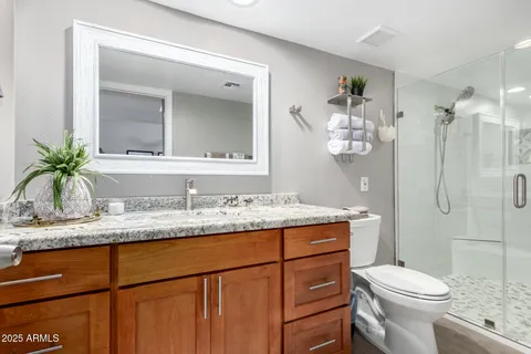 a bathroom with a granite countertop sink toilet mirror and a shower