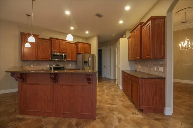 a kitchen with stainless steel appliances granite countertop a refrigerator a stove top oven and a sink with wooden cabinets