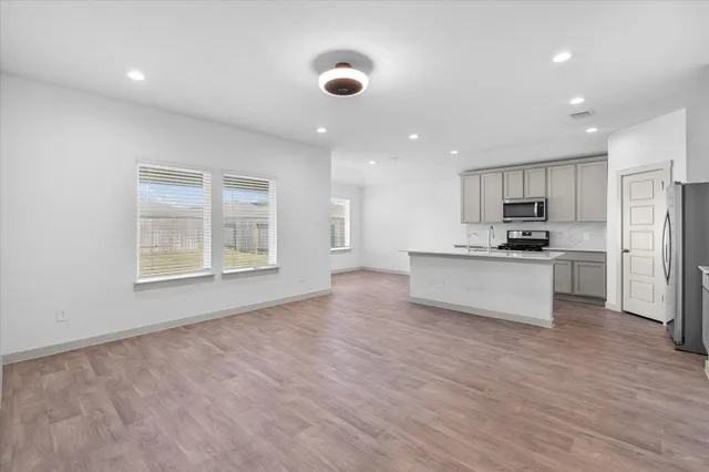 a kitchen with stainless steel appliances granite countertop a stove a sink a refrigerator white cabinets and wooden floor next to a window