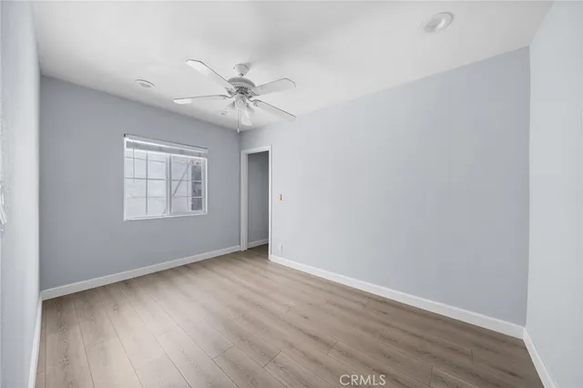 an empty room with wooden floor ceiling fan and windows