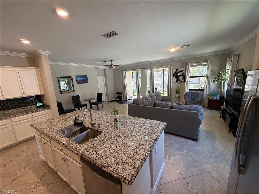 Kitchen featuring stainless steel appliances, crown molding, light stone countertops, backsplash, and a kitchen island with sink