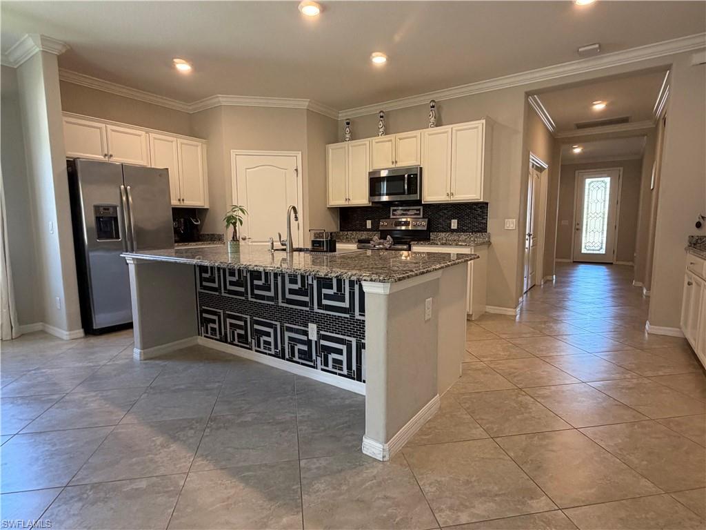 4284 Raffia Palm Circle Naples, FL 34119 - Photo 4 of 50 Kitchen with stainless steel appliances, white cabinetry, dark stone counters, ornamental molding, and a kitchen island with sink