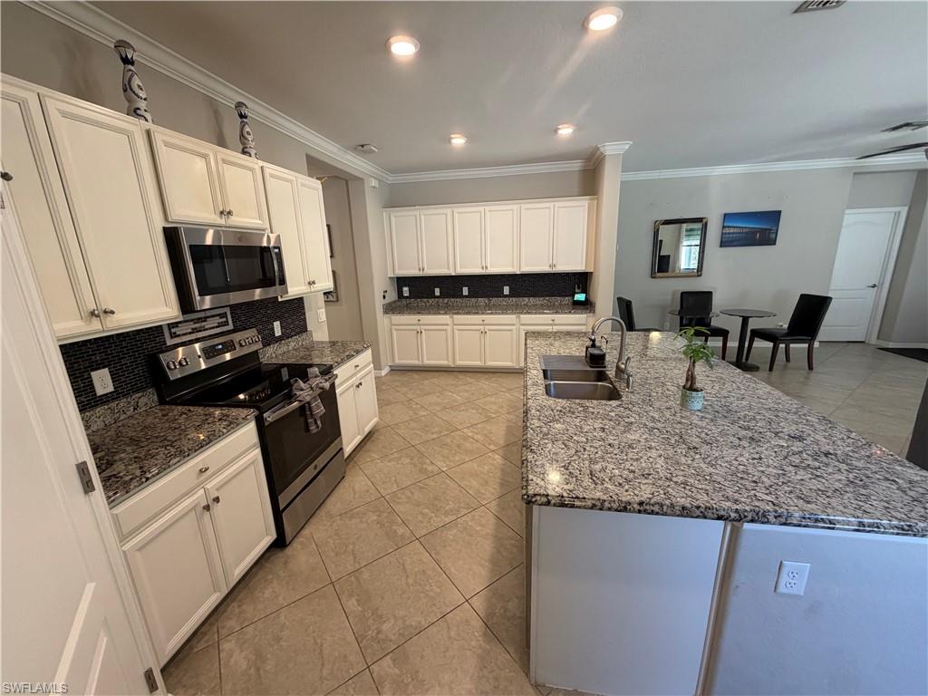 4284 Raffia Palm Circle Naples, FL 34119 - Photo 5 of 50 Kitchen featuring stainless steel appliances, light tile patterned floors, white cabinets, dark stone countertops, and tasteful backsplash