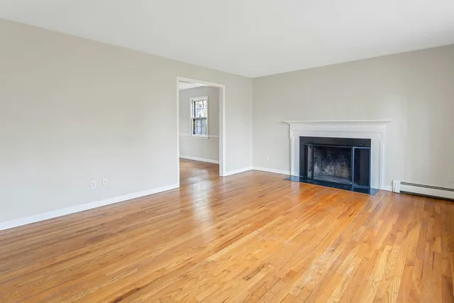 a view of an empty room with wooden floor fireplace and a window