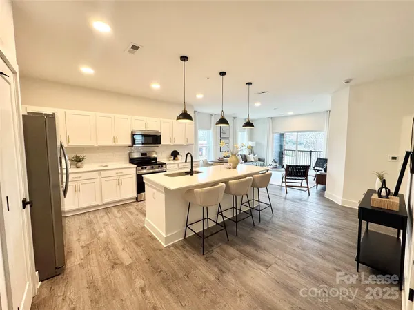 a kitchen with stainless steel appliances kitchen island granite countertop a refrigerator a stove a sink a dining table and chairs with wooden floor