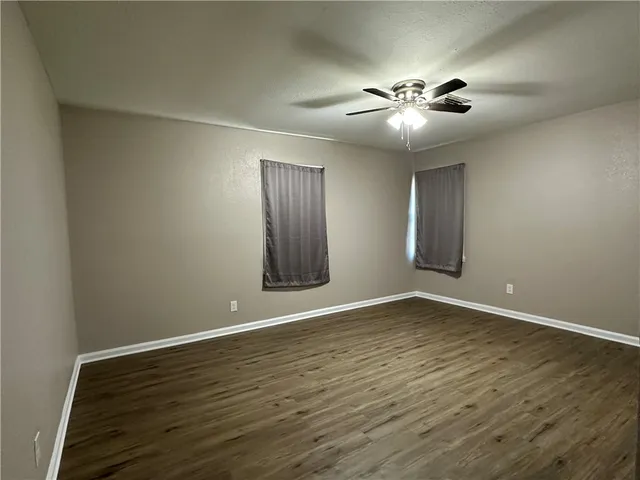 a view of an empty room with wooden floor and fan
