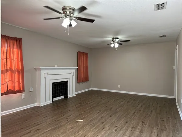 a view of an empty room with a fireplace a ceiling fan and wooden floor
