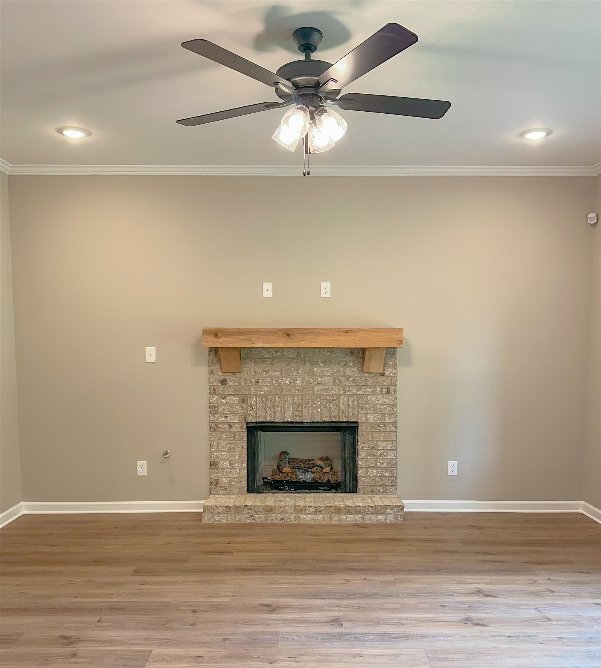 126 Stewart Road Munford, TN 38058 - Photo 7 of 23 Unfurnished living room featuring hardwood / wood-style floors, ceiling fan, crown molding, and a brick fireplace