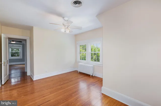 an empty room with wooden floor chandelier fan and windows