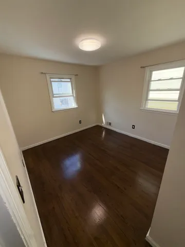 an empty room with wooden floor cabinet and windows
