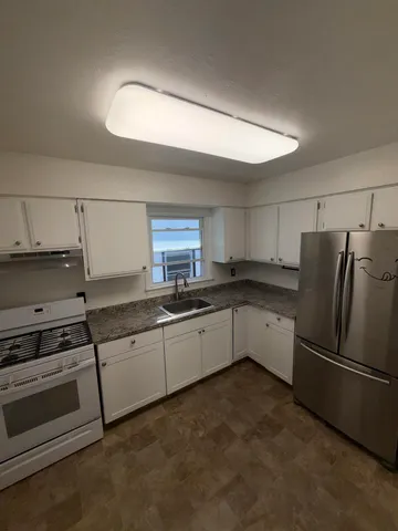 a kitchen with granite countertop a refrigerator and white cabinets