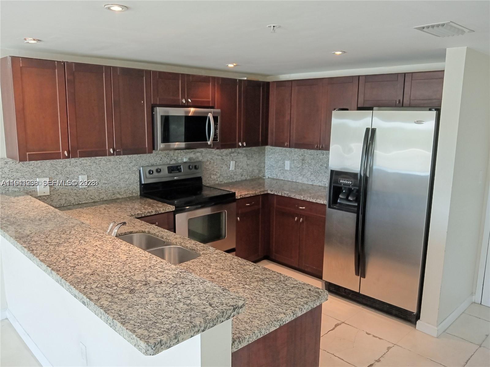 2740 Southwest 28th Terrace, Unit 507 Miami, FL 33133 - Photo 15 of 29 a kitchen with granite countertop wooden cabinets a refrigerator and a sink