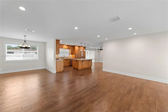 an empty room with wooden floor kitchen and windows