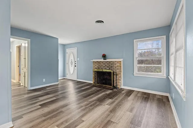a view of an empty room with wooden floor fireplace and a window