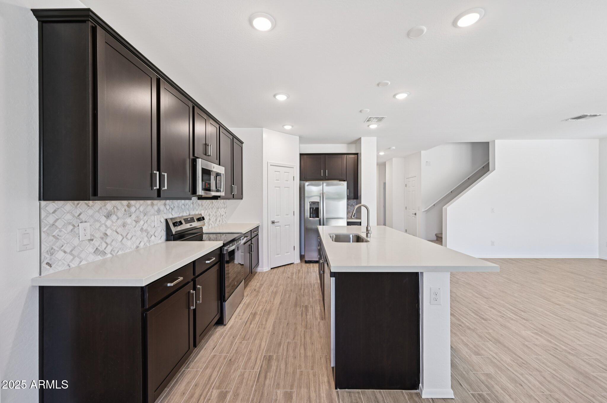 5535 South 240th Lane Buckeye, AZ 85326 - Photo 12 of 57 a kitchen with stainless steel appliances kitchen island granite countertop a refrigerator a sink dishwasher a stove and a dining table with wooden floor