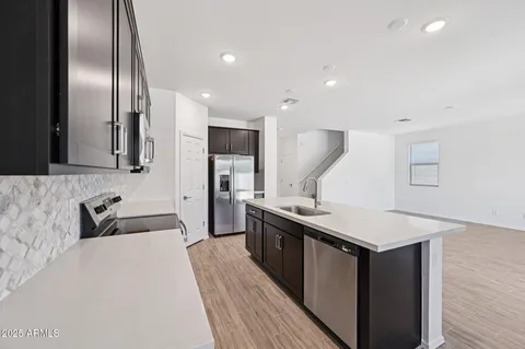 a kitchen with stainless steel appliances a sink dishwasher a stove top oven a refrigerator with wooden floor and cabinets