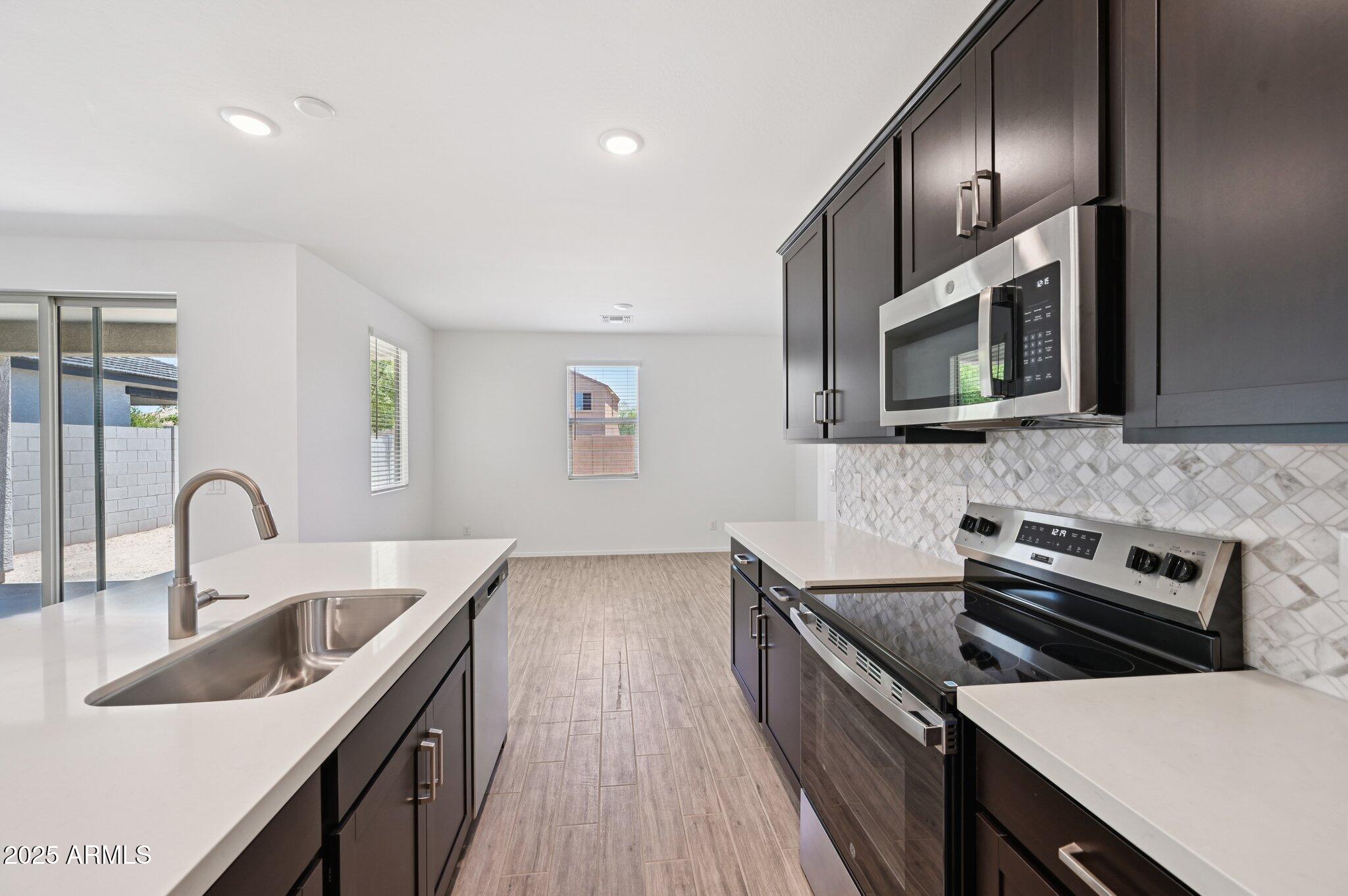 5535 South 240th Lane Buckeye, AZ 85326 - Photo 14 of 57 a kitchen with stainless steel appliances a sink dishwasher a stove top oven a refrigerator with wooden floor and cabinets
