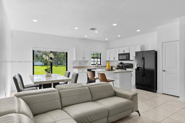 a living room with stainless steel appliances furniture windows and a kitchen view