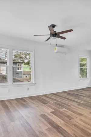 an empty room with wooden floor fan and windows