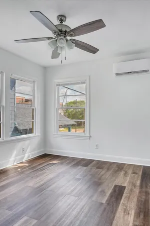 an empty room with wooden floor ceiling fan and windows