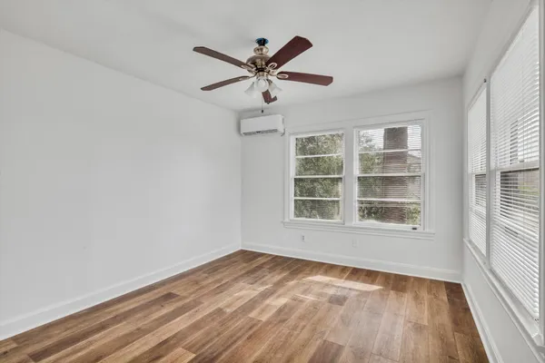 an empty room with wooden floor fan and windows
