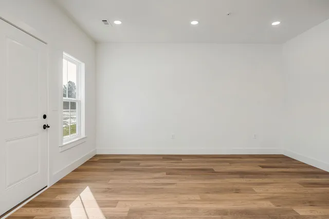 a view of an empty room with a window and wooden floor