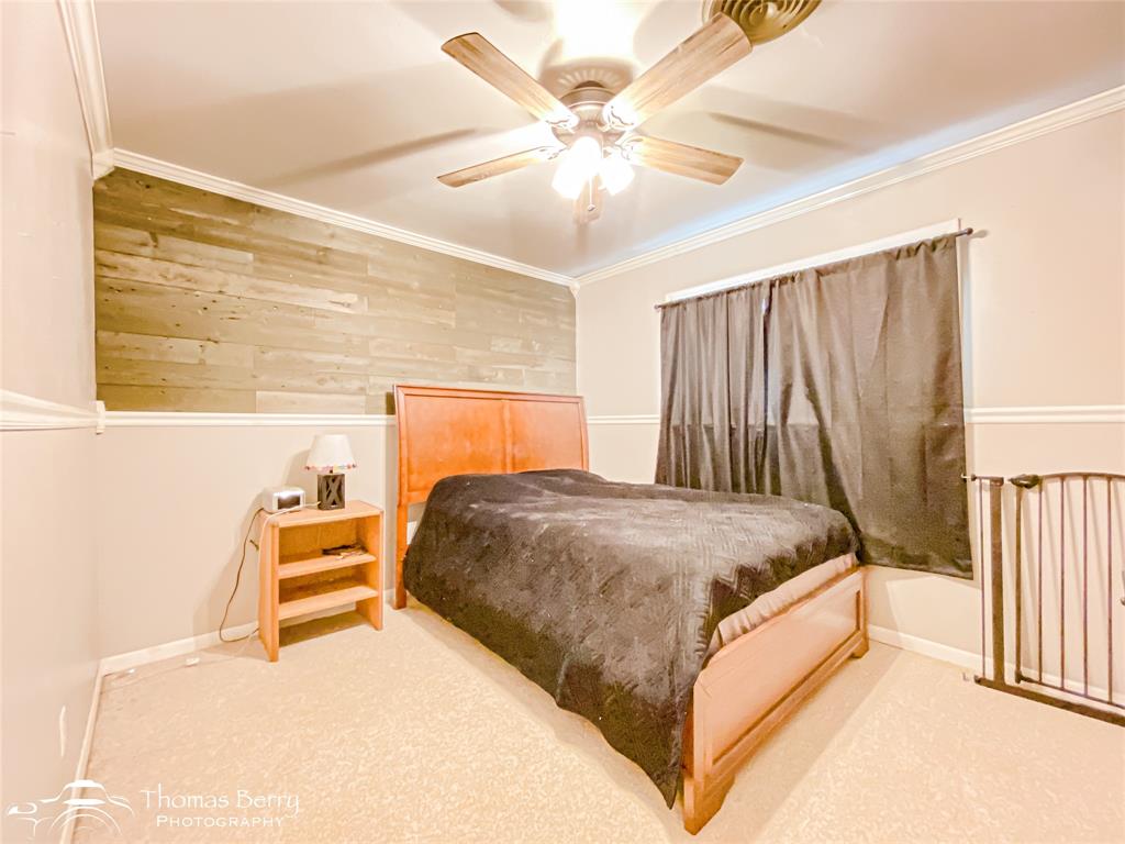 1104 Hickory Street Roscoe, TX 79545 - Photo 14 of 22 Bedroom with a ceiling fan, ornamental molding, wooden walls, and carpet flooring