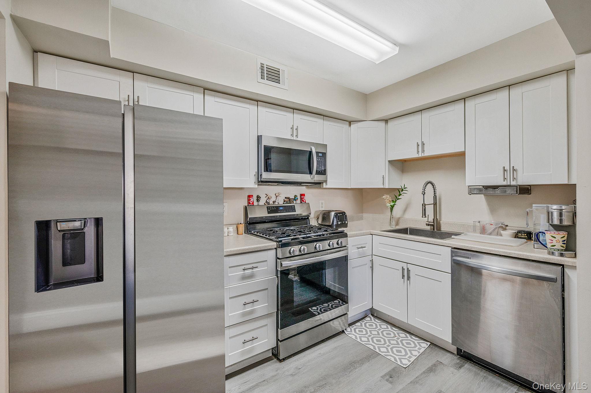 63 Rocky Point Yaphank Road, Unit 80 Rocky Point, NY 11778 - Photo 8 of 25 Kitchen with stainless steel appliances, white cabinets, and light wood-style floors