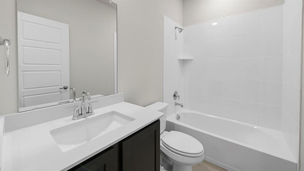 412 Carthage Street Caddo Mills, TX 75135 - Photo 30 of 32 Bathroom featuring a white integrated sink with a chrome faucet, dark wood-finish vanity, large wall mirror, and a white bathtub with tile surround